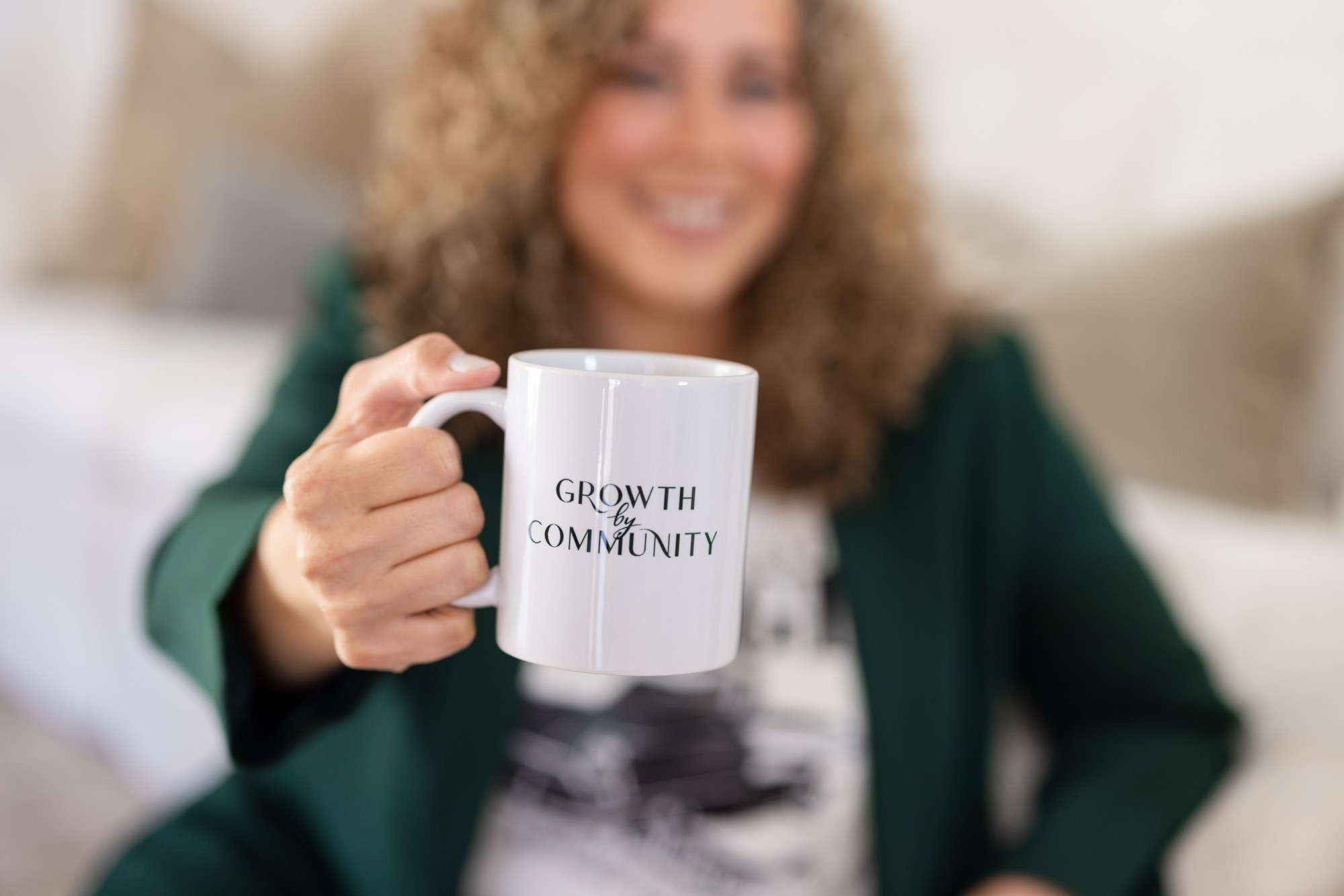 Person holding a white mug with text, smiling, in a cozy indoor setting.