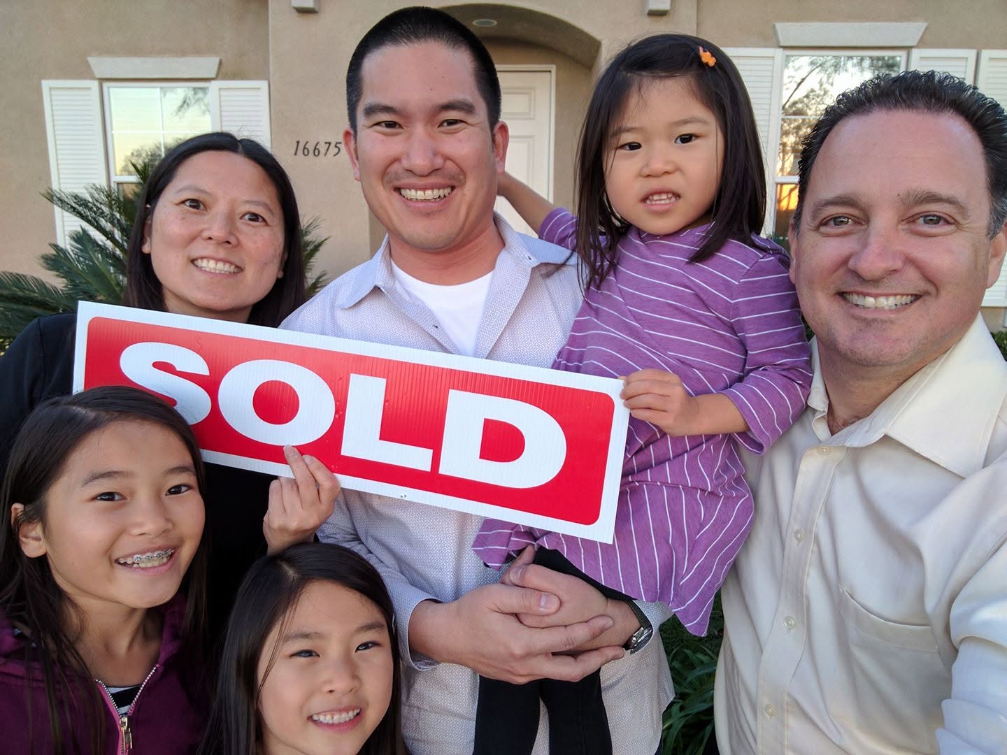 Group of five people smiling outdoors, holding a 'SOLD' sign, with a house in the background.