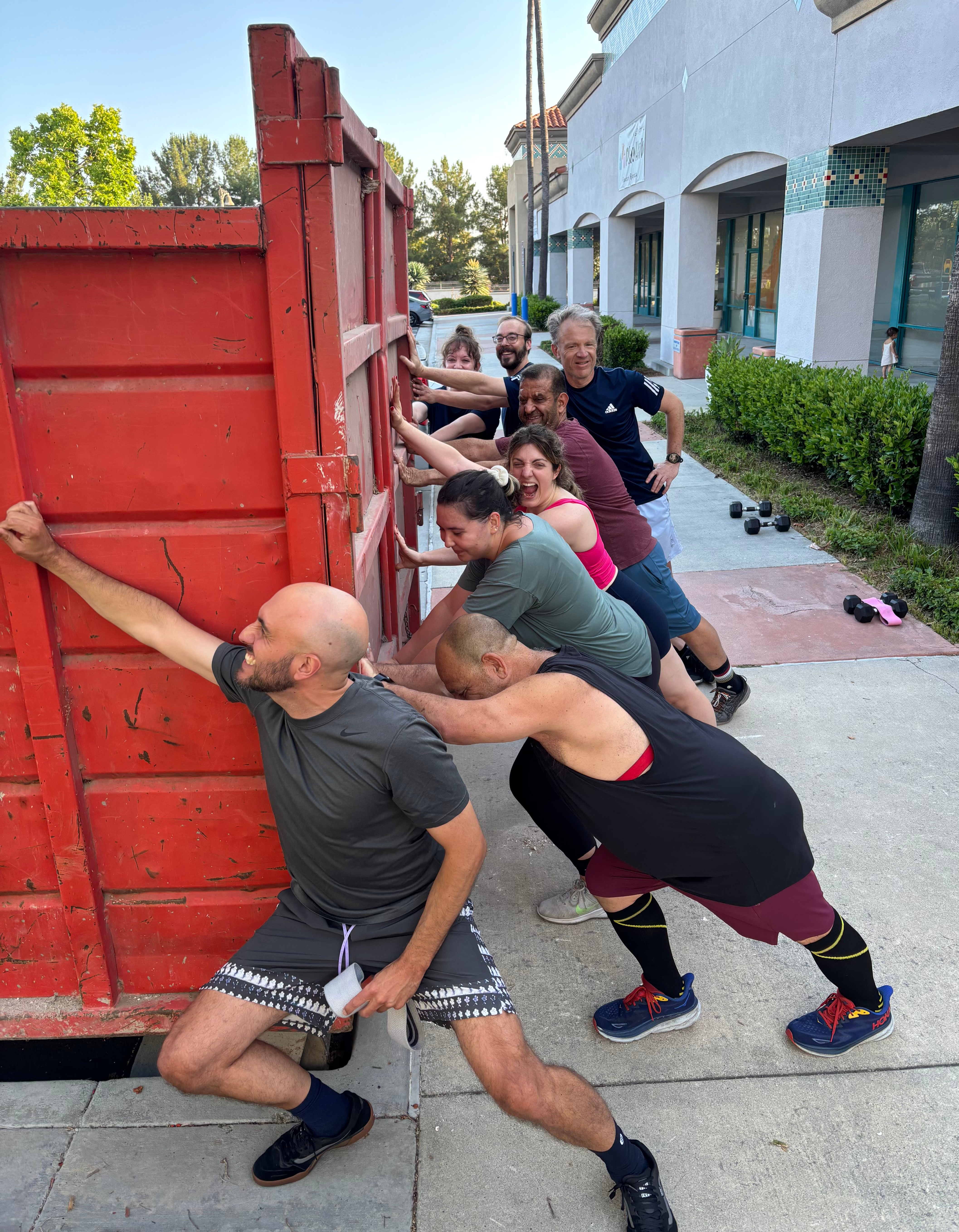 Group of people pulling a red wooden fence on a sidewalk, with buildings and greenery in the background.