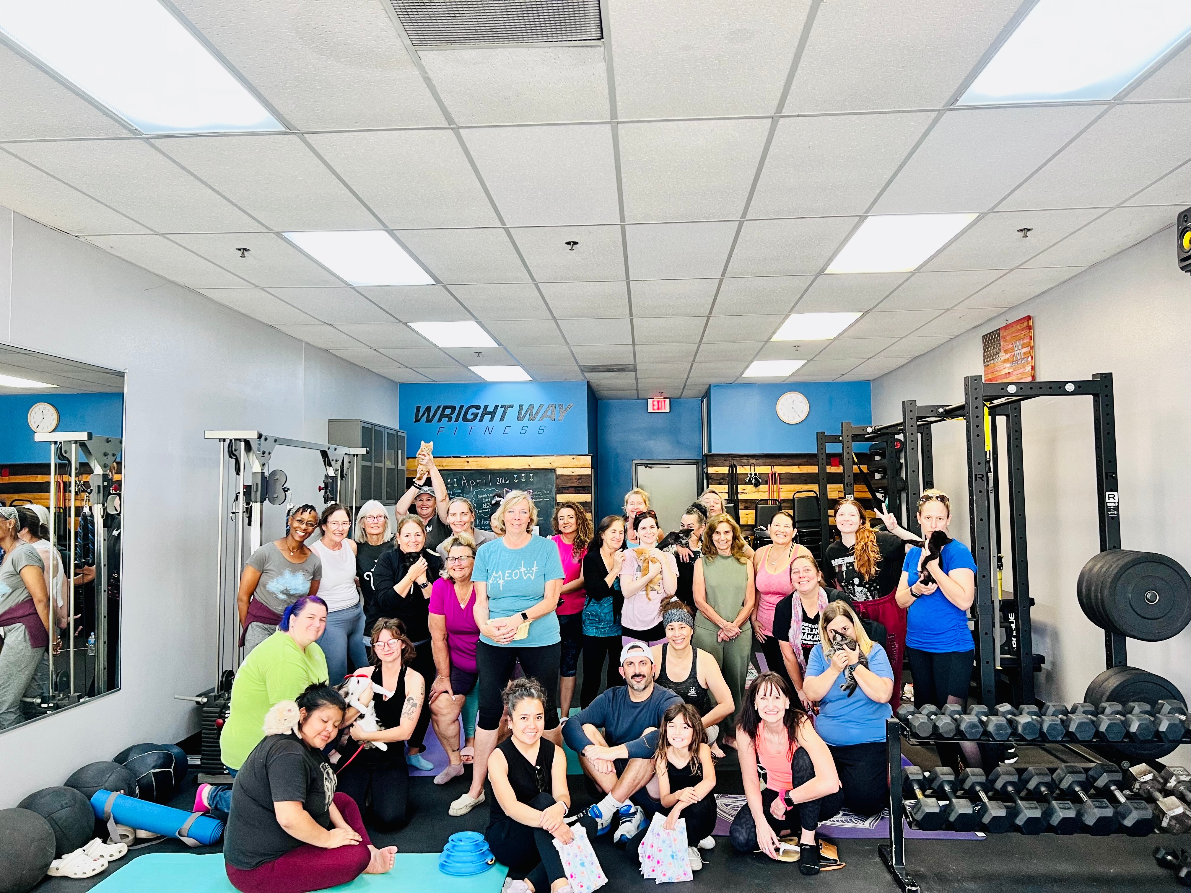 Group of people in a gym, some sitting and some standing, with workout equipment around them.