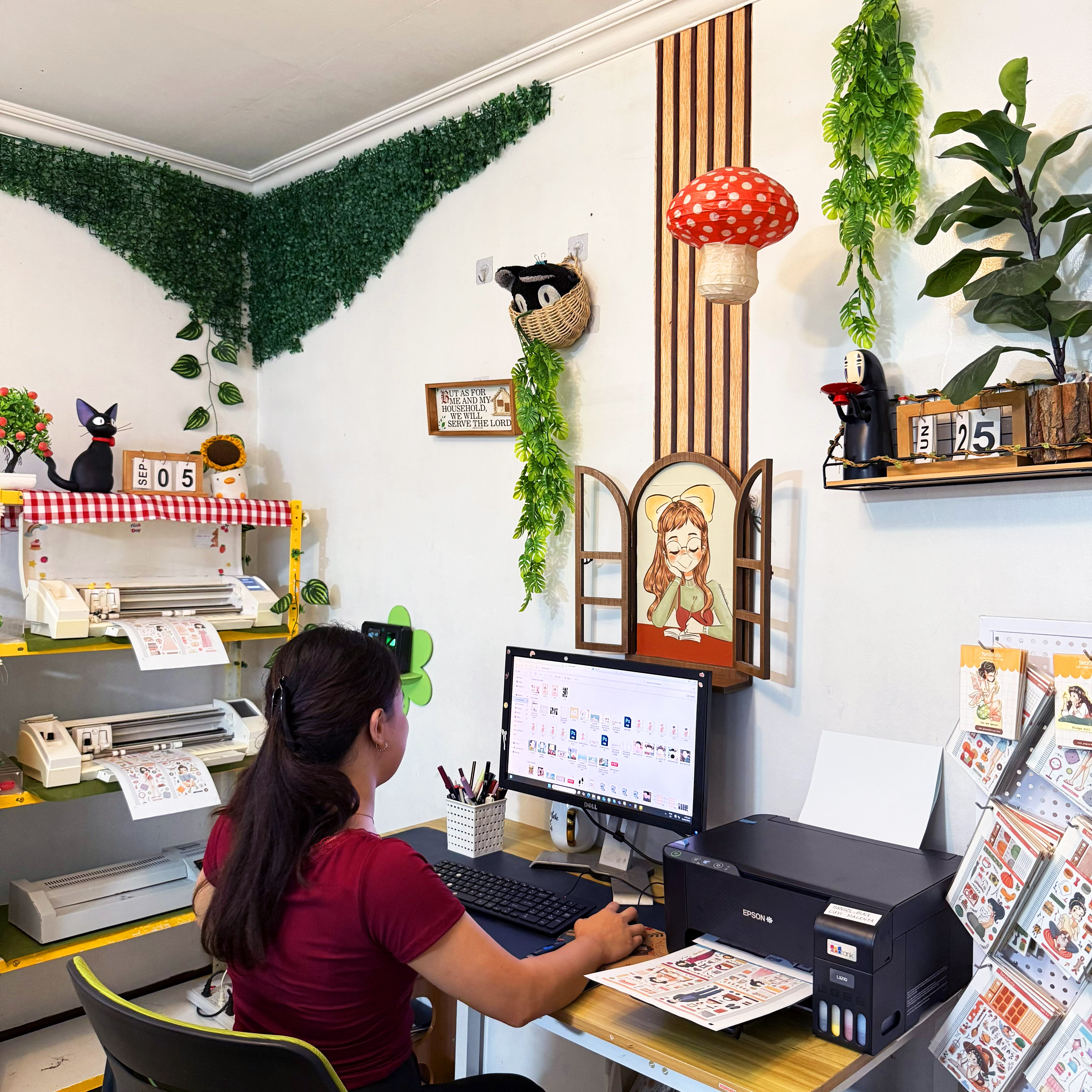 Woman working at a desk with a computer in a decorated room with plants and artwork.
