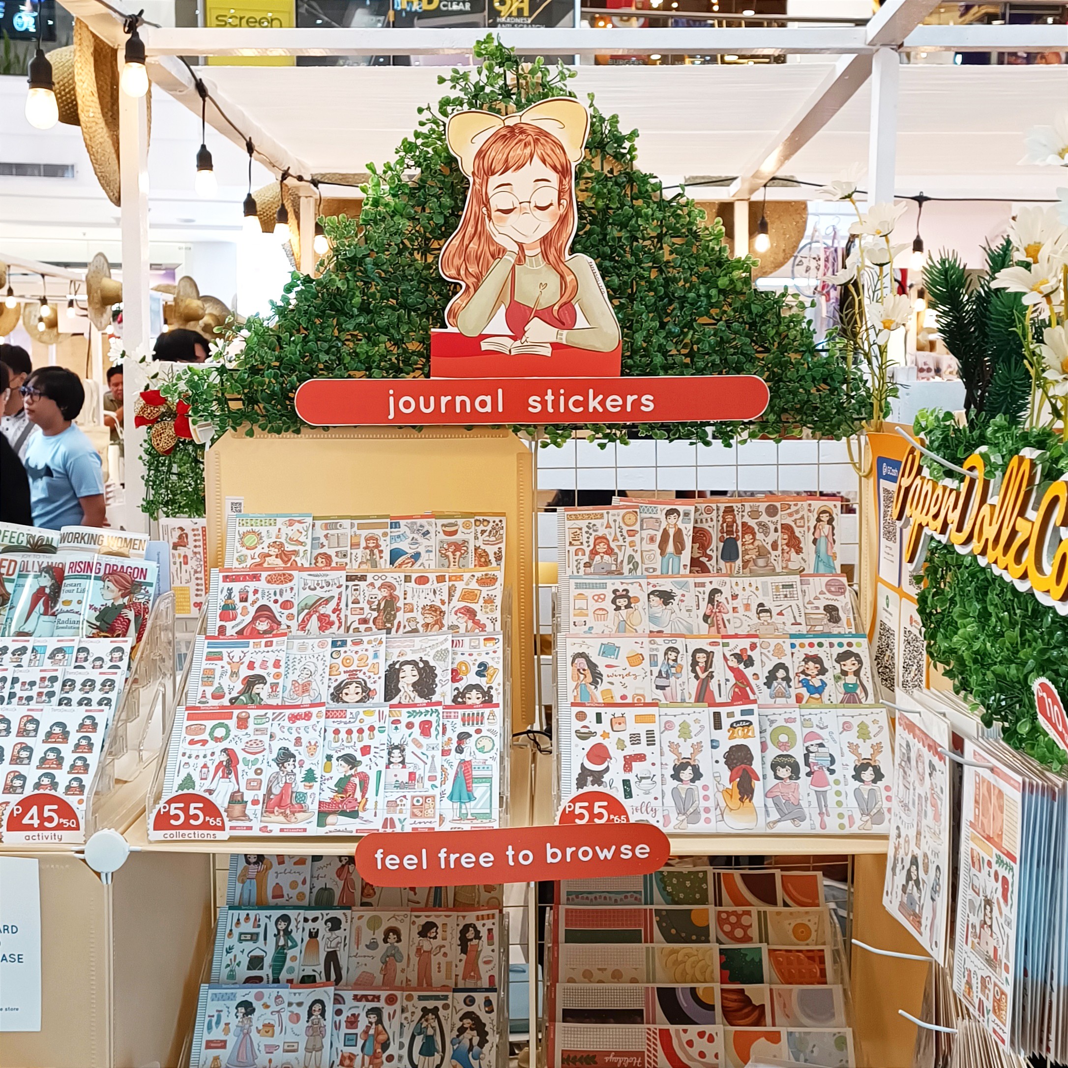 Display of journal stickers with a cartoon girl and greenery, with signs reading 'journal stickers' and 'feel free to browse'.
