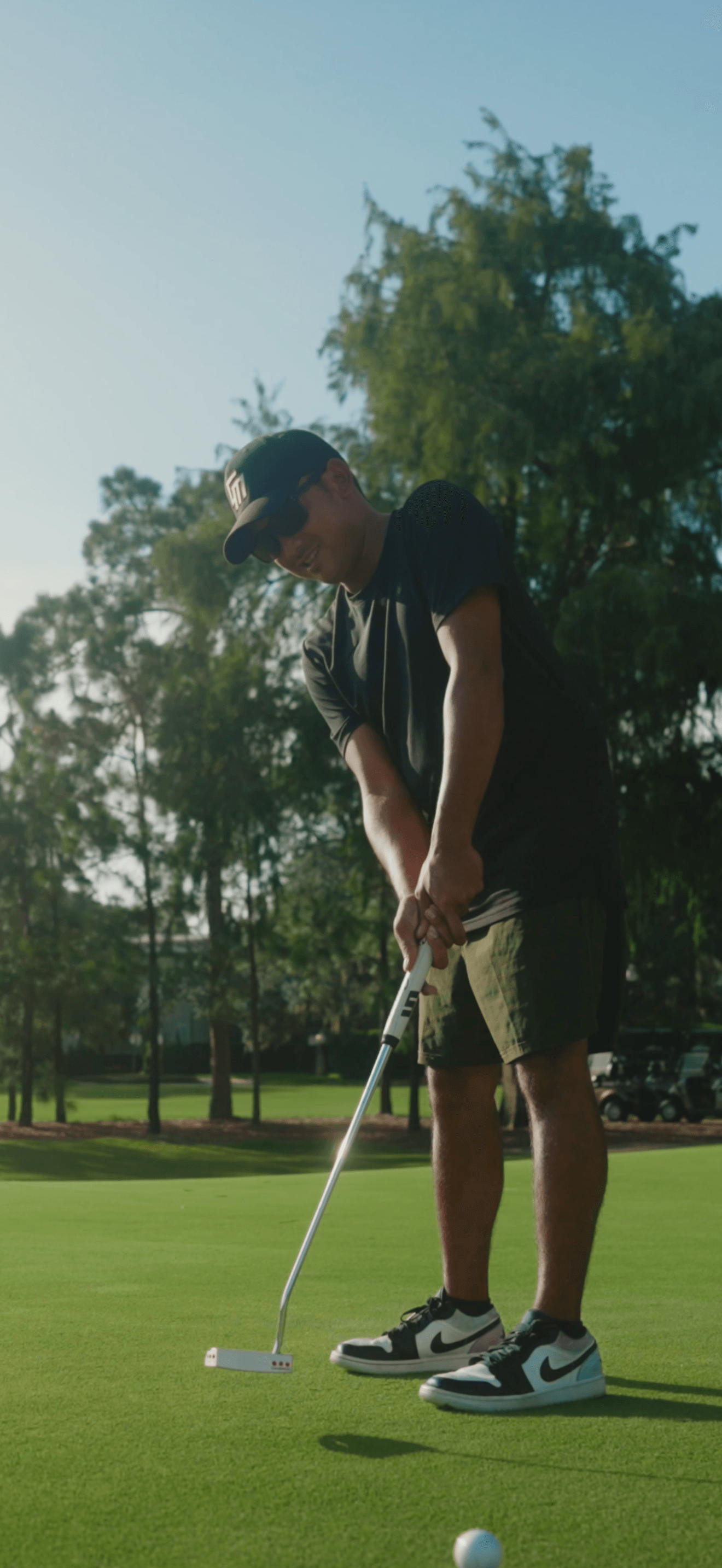 Person preparing to putt on a golf course with trees in the background.
