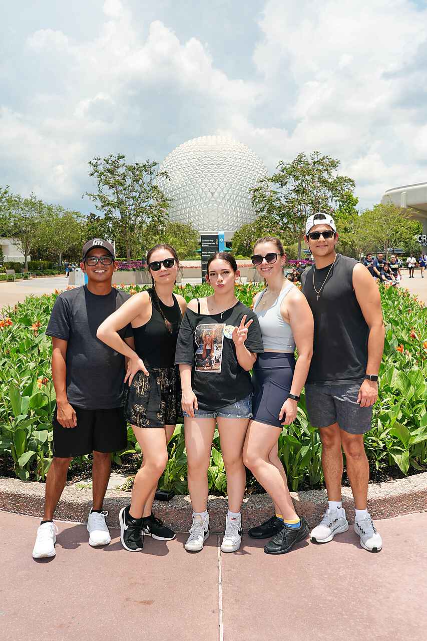Group of five people standing outdoors with a large spherical structure in the background, smiling and posing for the photo.