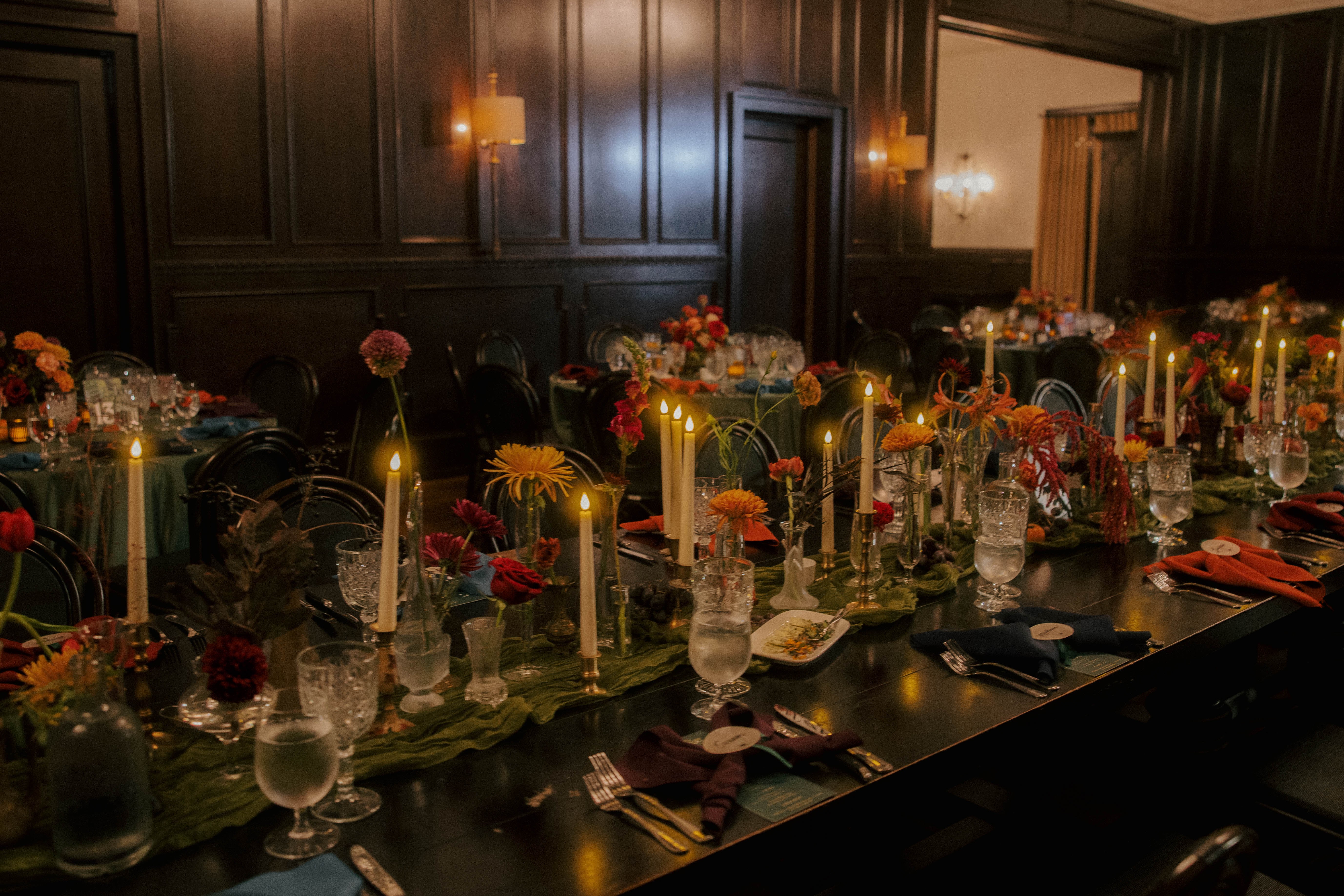 Elegant dining table with floral arrangements, candles, and tableware in a dark-paneled room.