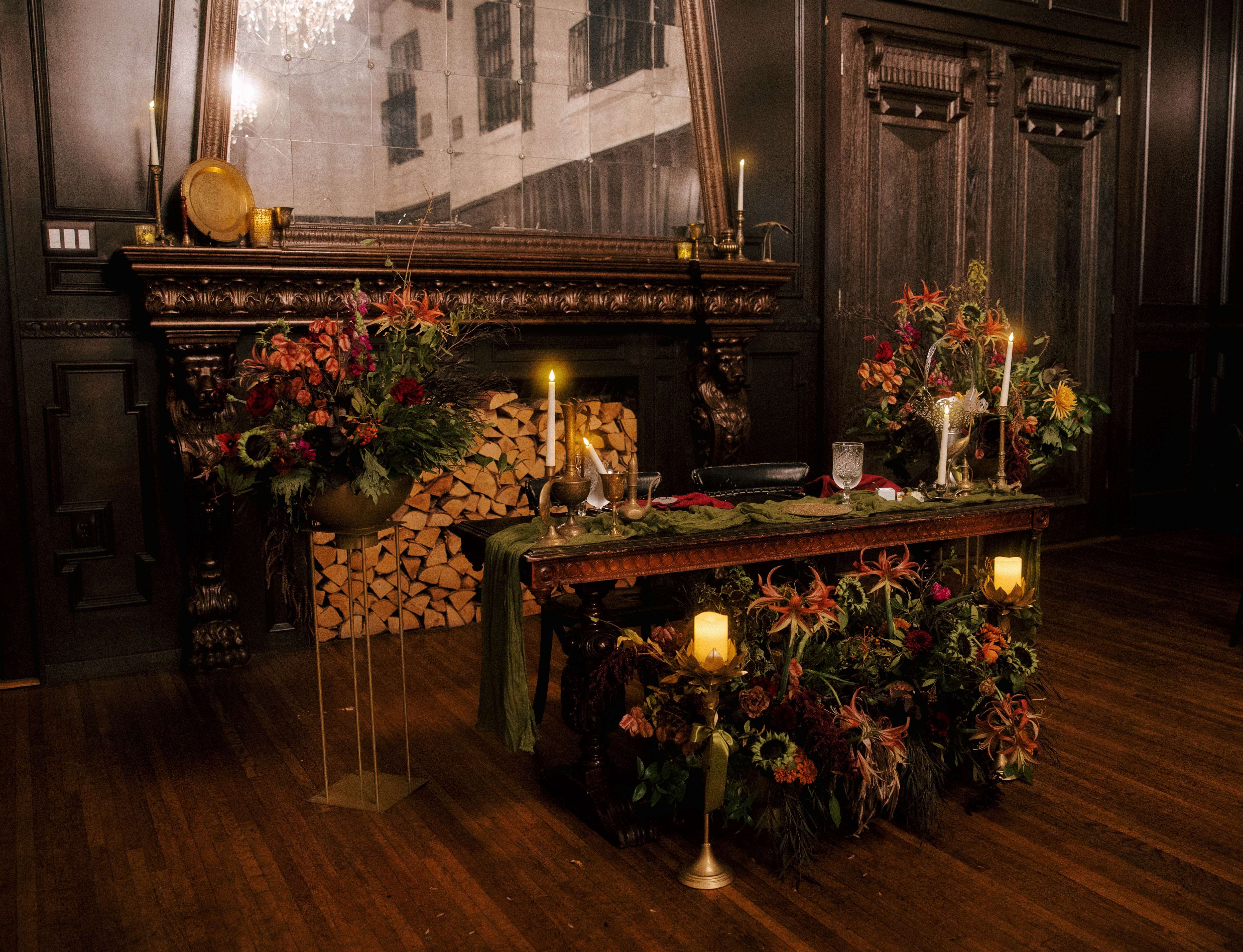 Decorative table with candles, flowers, and wood logs in a dimly lit room with dark wood paneling.