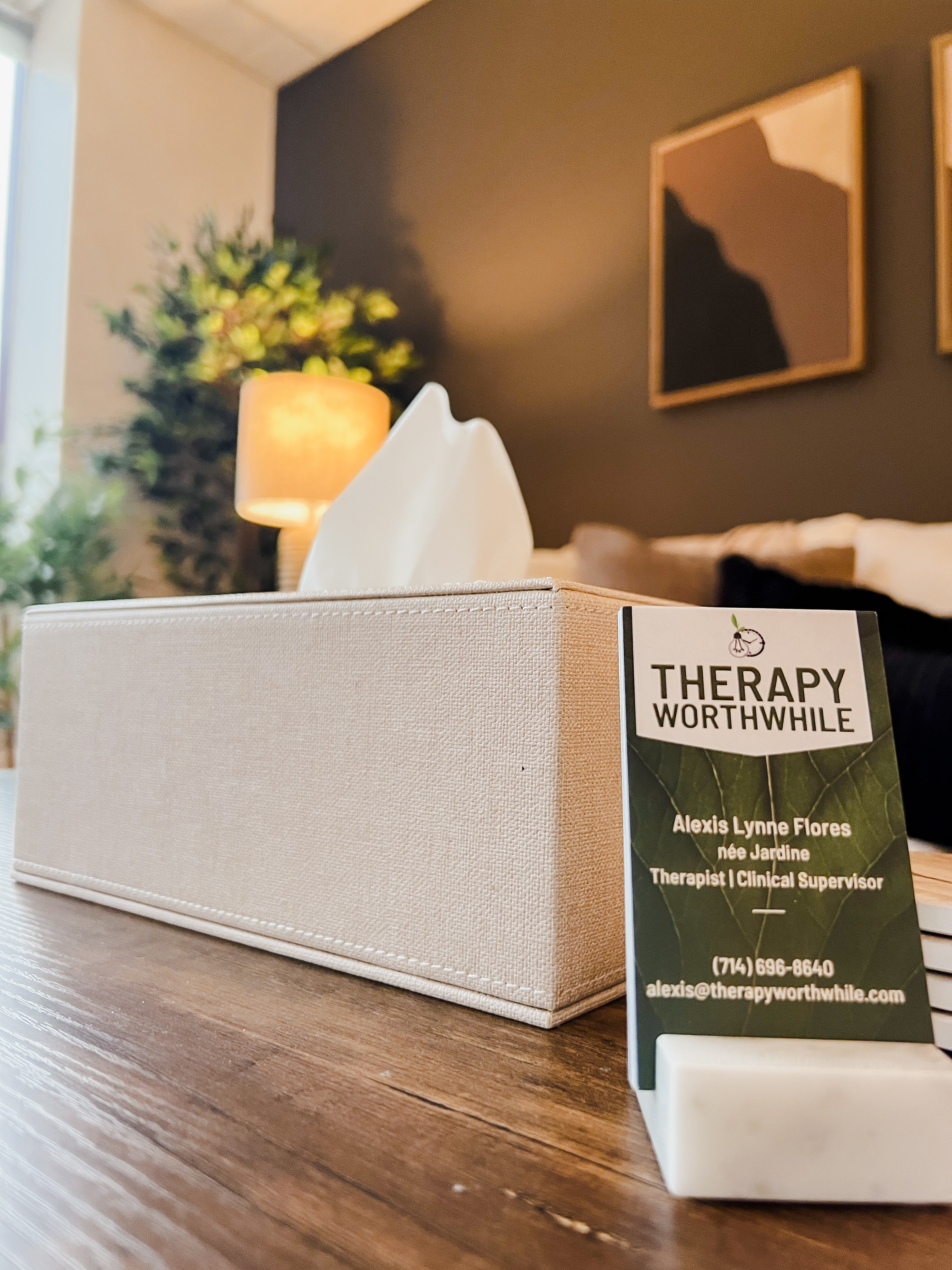 Box of tissues on a wooden table with a blurred background of a lamp, plant, and wall art.