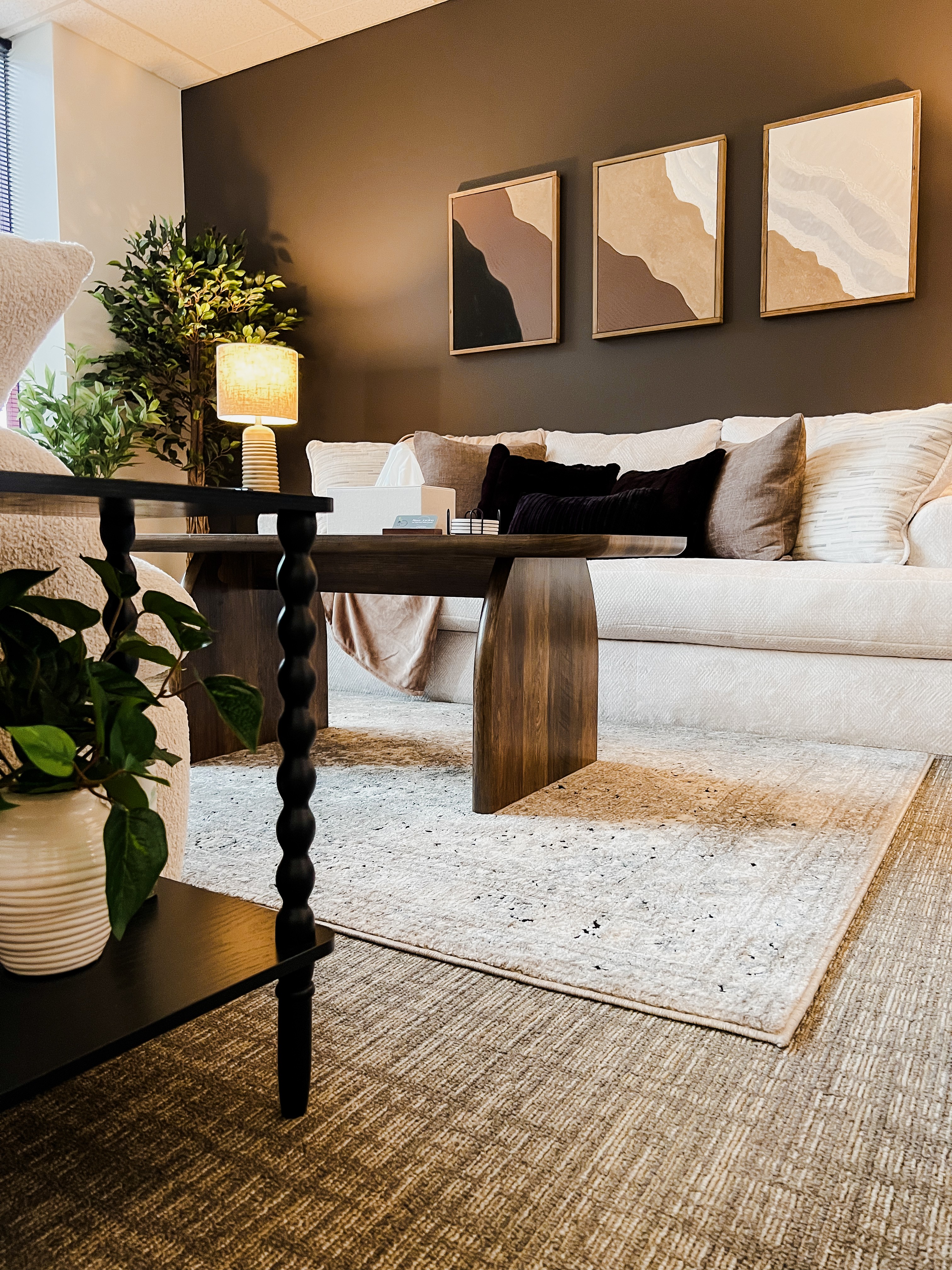 Living room with beige sofa, wall art, and a side table with a lamp, plants, and a rug.